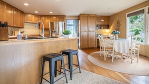 A modern kitchen with wooden cabinets, a central island with stools, and a dining area with a table and chairs.