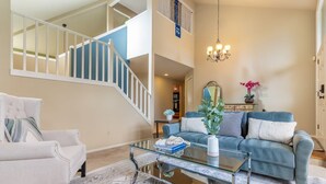 A spacious living room with a staircase, a glass coffee table, a blue sofa, and a white armchair.