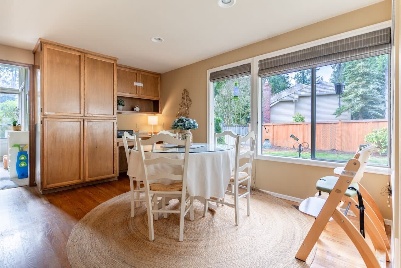 A kitchen with wooden cabinets, a dining table with chairs, and a large window with a view of a backyard.