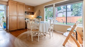 A kitchen with wooden cabinets, a dining table with chairs, and a large window with a view of a backyard.