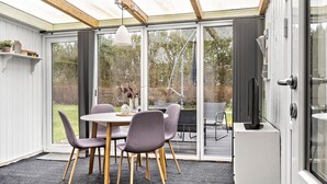 A conservatory with a dining table, chairs, and a television.