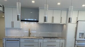 A modern kitchen with white cabinets, a marble countertop, and pendant lighting.