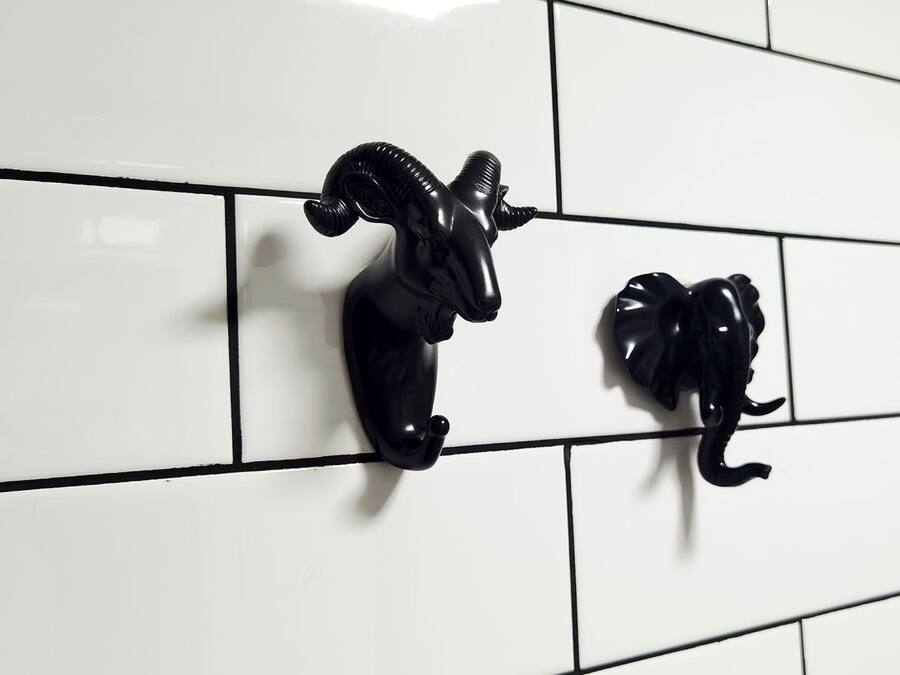 Two black wall-mounted animal figurines on a white tiled wall.