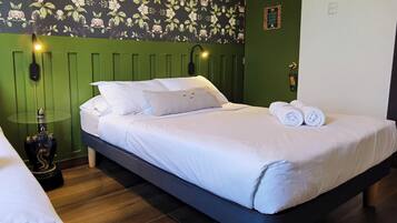 Ein ordentlich bezogenes Bett mit weißen Leinen und zwei aufgerollten Handtüchern, eine grüne Wand mit Blumenwallpaper und eine Wandlampe.