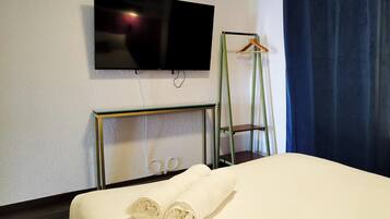 A hotel room with a bed, a TV mounted on the wall, a mirror, and a hanging coat rack.