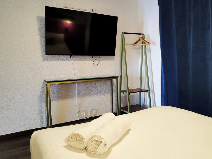A hotel room with a bed, a TV mounted on the wall, a mirror, and a hanging coat rack.