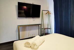 A hotel room with a bed, a TV mounted on the wall, a mirror, and a hanging coat rack.