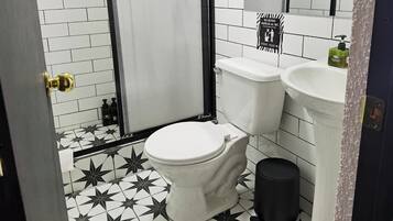 A bathroom with a white toilet, a black trash bin, a sink, and a shower area.
