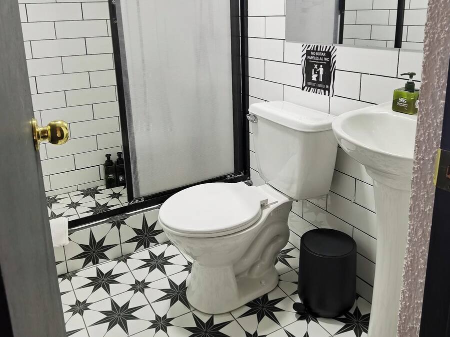 A bathroom with a white toilet, a black trash bin, a sink, and a shower area.
