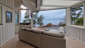 Una habitación acogedora con un ventanal grande con vistas a un lago, un sofá color beige y suelo de madera.