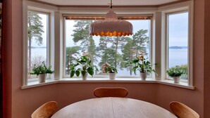Un comedor con ventanal panorámico que da a un lago, con una mesa y sillas de madera, y plantas en macetas en el alféizar.