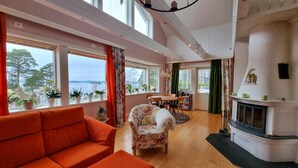 Un salón espacioso con un sofá naranja grande, un sillón estampado y una chimenea. Varias ventanas ofrecen vistas al exterior.