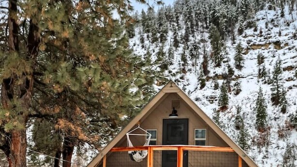 Una cabaña de dos pisos con balcón, rodeada de árboles nevados y cielo despejado.