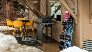 Una cabaña con balcón, un comedor con sillas amarillas, una parrilla y una tabla de snowboard apoyada en la pared.