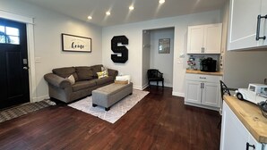 Un salon moderne avec un parquet en bois foncé, un canapé gris et une grande lettre décorative en forme de « S ».