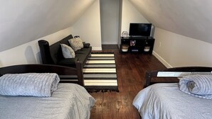 Une petite chambre mansardée de forme triangulaire, avec deux lits, un canapé, une télévision et un plancher en bois.