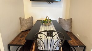 Un coin repas comprenant une table rectangulaire, deux chaises et un téléviseur fixé au mur, juste au-dessus.