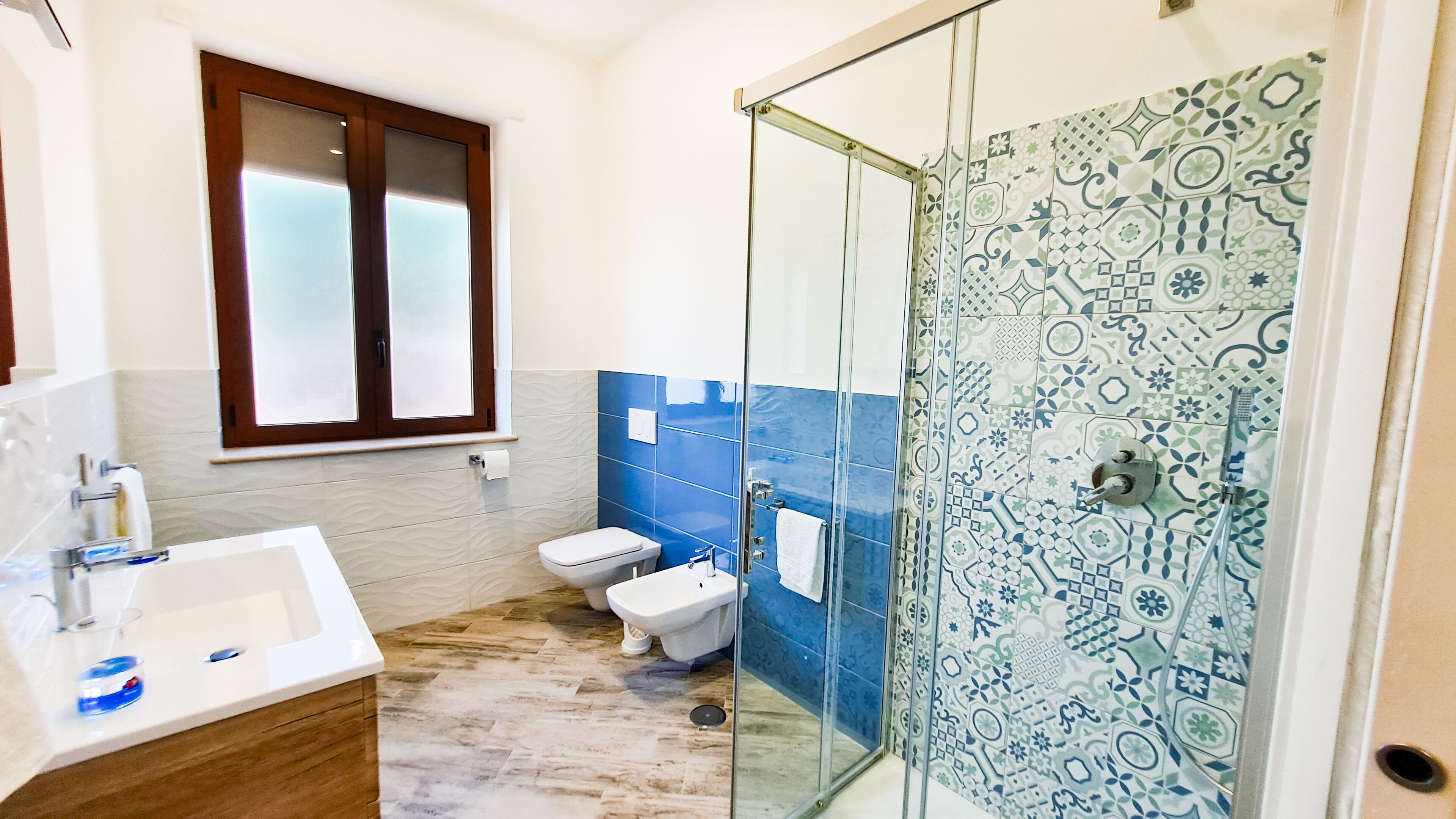 Baño con cabina de ducha de vidrio, inodoro, lavamanos y ventana con vidrio esmerilado.