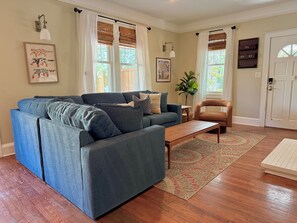 Ein Wohnzimmer mit einem blauen Ecksofa, einem Holztisch, einem braunen Sessel und einem gemusterten Teppich.