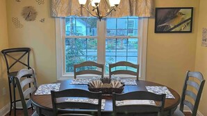 A dining room with a round table, six chairs, a chandelier, a window with a view, and wall decorations.