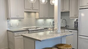 A modern kitchen with white cabinetry, a granite countertop, a central island with stools, and pendant lighting.