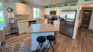 A modern kitchen with white cabinetry, stainless steel appliances, and a central island with two stools.