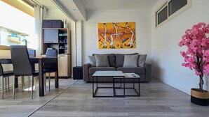 En moderne stue med sofa, sofabord og stole. Et maleri hænger på væggen, og der står en potteplante.
