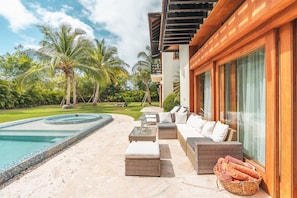 A poolside area with a lounge, wicker furniture, and a view of the pool and surrounding greenery.