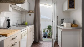 Cozinha compacta com cafeteira, pia e armários. Uma cortina divide a cozinha de uma varanda com plantas em vasos.