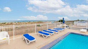A poolside area with sun loungers, a pool, and a view of the beach.