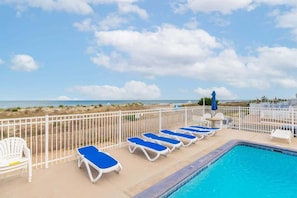 Uma área à beira da piscina com espreguiçadeiras, piscina e vista para a praia.