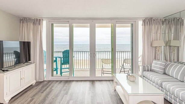 A room with a large sliding glass door leading to a balcony, a white sofa, a small table, and a TV on a cabinet.