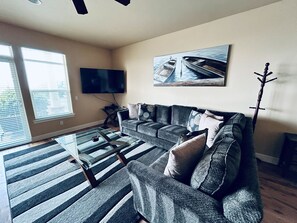A living room with a sofa, a coffee table, a flat-screen TV, and a painting on the wall.