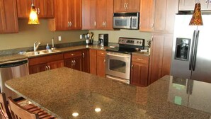 Eine Küche mit Granit Arbeitsplatten, Holzschränken, Edelstahlgeräten und Pendelleuchten.
