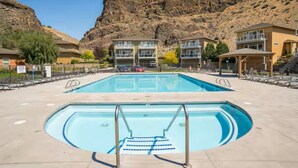 Una piscina con trampolino, circondata da edifici con balconi, con montagne sullo sfondo.