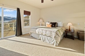 Ein Schlafzimmer mit einem großen Bett, zwei Nachttischen, Blick auf eine gebirgige Landschaft durch eine Schiebeglastür und einem Teppichboden.