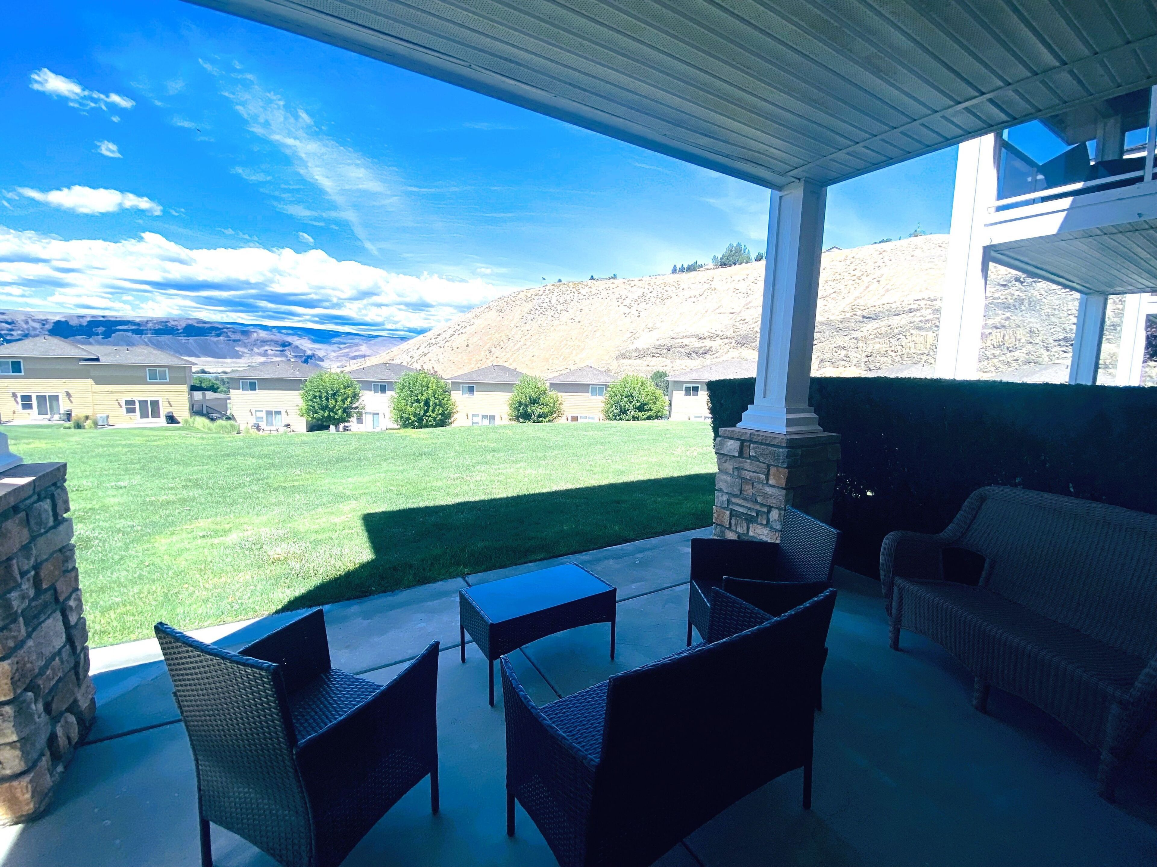 An outdoor patio with wicker furniture, a stone pillar, and a view of a residential area with houses and hills.