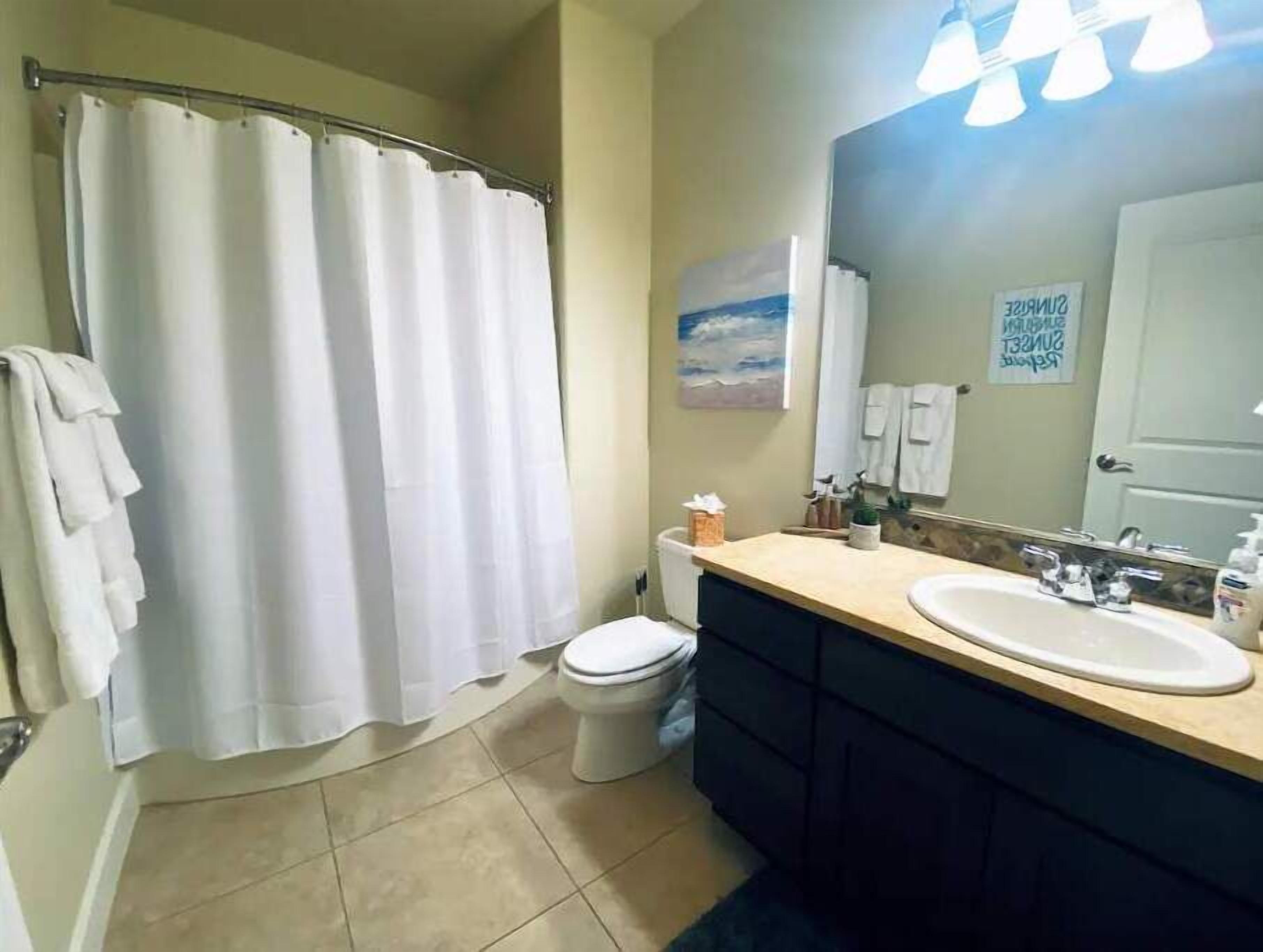 Un baño con cortina de ducha, inodoro, lavamanos y espejo.