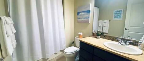 Un baño con cortina de ducha, inodoro, lavamanos y espejo.