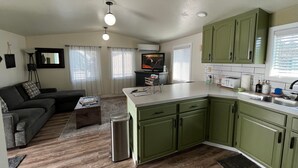 A compact living space with a kitchenette, a sofa, a coffee table, and a TV. - Cozy Downtown Sitka Home, Car Rental Option (Sitka)