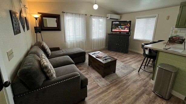 A compact living space with a sofa, coffee table, and a TV. There is a kitchen area with a counter and a trash bin. - Cozy Downtown Sitka Home, Car Rental Option (Sitka)