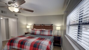 A bedroom with a bed, two bedside tables with lamps, a ceiling fan, a window with blinds, and a door. - Red River Retreat (Red River)