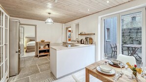 Une cuisine moderne dotée d’un îlot central, d’un coin repas avec une table dressée pour deux personnes et d’une vue sur la terrasse extérieure, accessible par une porte-fenêtre coulissante.