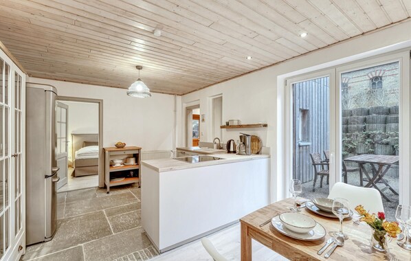 Een moderne keuken met een centraal eiland, een zithoek met een tafel gedekt voor twee personen, en uitzicht op het buitenterras door een schuifdeur van glas.