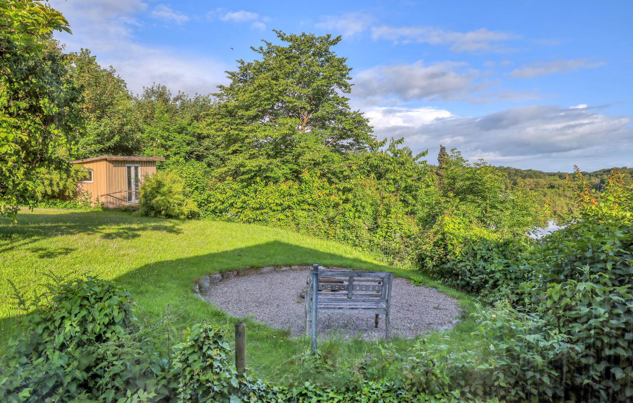 Un jardin avec un banc en bois, un petit abri de jardin et une végétation luxuriante.
