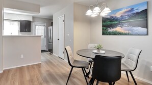 A modern kitchen with dark cabinets, a dining area with a round table and four chairs, and a large landscape painting on the wall. - Lafayette Townhouse Minutes from Good Samaritan Hospital (Lafayette)