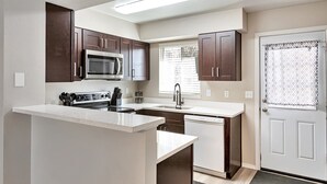 A compact kitchen with dark wooden cabinets, a stainless steel microwave, a built-in oven, and a white countertop. - Lafayette Townhouse Minutes from Good Samaritan Hospital (Lafayette)