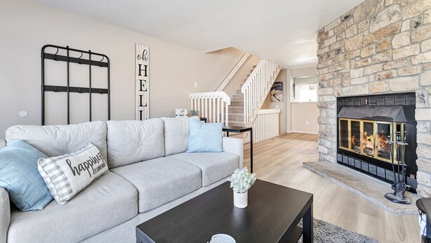 A modern living room with a stone fireplace, a grey sofa with decorative pillows, a black coffee table, and a staircase leading to another level. - Lafayette Townhouse Minutes from Good Samaritan Hospital (Lafayette)