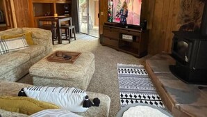 A cozy living room with a television, a fireplace, and a dining area with a table and chairs. - Doney Creek Cabin (Lakehead-Lakeshore)