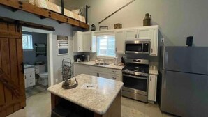 A compact kitchen with white cabinets, a stainless steel refrigerator, a microwave, and an oven. There is a small island with a sink and a coffee maker. - Doney Creek Studio (Lakehead-Lakeshore)